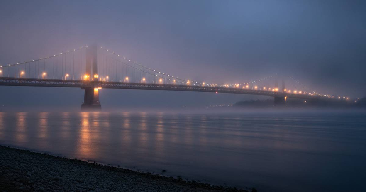 A lit suspension bridge disappearing into fog at dusk